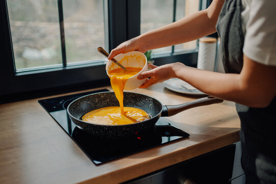Chef pouring whisked eggs into frying pan on induction stove top