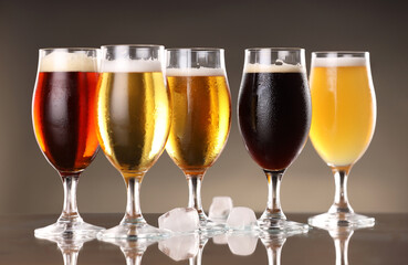 Glasses with different types of beer and ice cubes on mirror surface, closeup