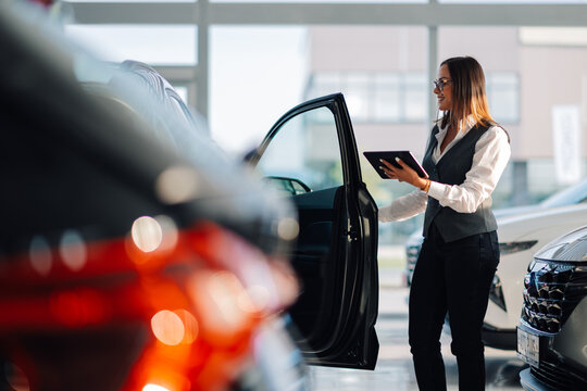 Car saleswoman presents a vehicle to a customer in the showroom.