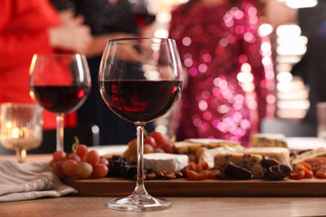 People holding glasses of wine at party, focus on wooden table with snacks and alcohol