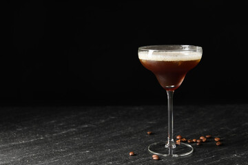 Glass of delicious espresso martini and coffee beans on dark textured table. Space for text