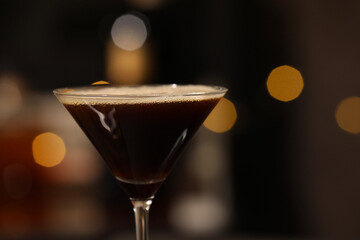 Delicious espresso martini in glass against blurred lights, closeup