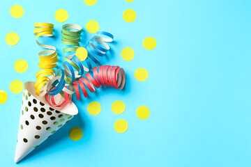 Party hat with confetti and streamers on light blue background, flat lay. Space for text