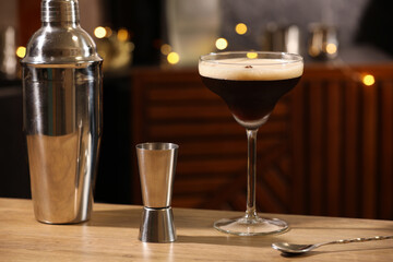 Glass with delicious espresso martini, jigger and shaker on wooden table in bar