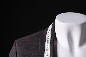 Male mannequin with jacket and measuring tape on black background, closeup