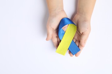 Child with yellow and blue ribbon on white background, top view. Down syndrome awareness