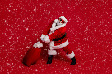 Photo of funny tired santa claus wear red headwear hat dark glasses dragging red sack isolated red color background