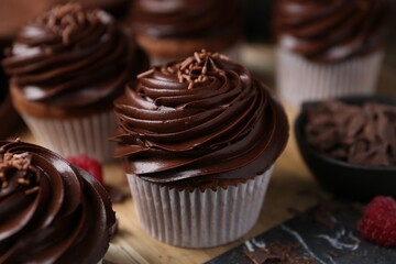 Tasty cupcakes with chocolate cream and raspberries on wooden table, closeup