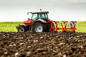 Tractor with plow attachment turns the soil in a vast, green farmland