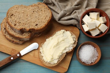 Fresh bread with butter, salt and knife on blue wooden table, flat lay