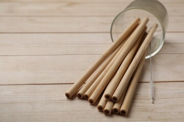 Bamboo drinking straws and cleaning brush on wooden table, closeup. Space for text
