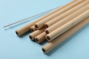 Bamboo drinking straws and cleaning brush on light blue background, closeup