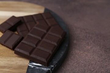 Pieces of delicious dark chocolate on brown table, closeup. Space for text