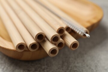 Bamboo drinking straws and cleaning brush on grey textured table, closeup