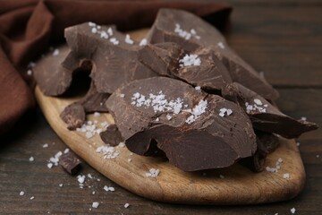 Pieces of chocolate with salt on wooden table, closeup