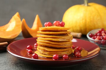 Tasty pumpkin pancakes with cranberries and honey on grey table, closeup