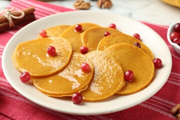 Tasty pumpkin pancakes with honey and cranberries on table, closeup