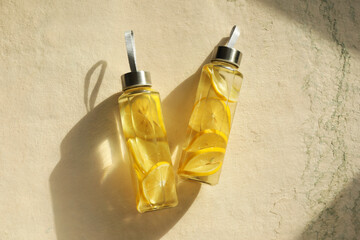 Lemon water in bottles on beige textured background, top view