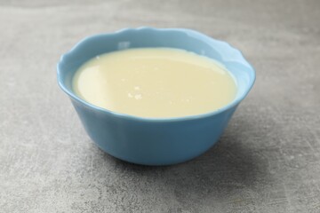 Condensed milk in bowl on light grey table, closeup