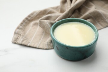 Condensed milk in bowl on white marble table, closeup. Space for text