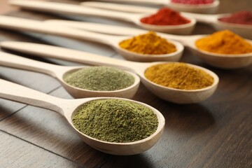 Different aromatic spices in spoons on wooden table, closeup