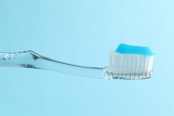Toothbrush with toothpaste in air on light blue background, closeup