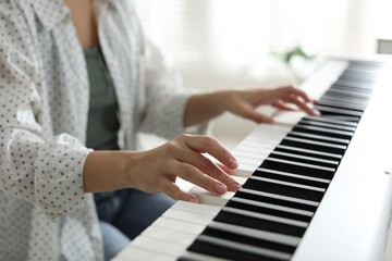 Woman playing synthesizer indoors, closeup. Electronic musical instrument