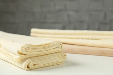 Stack of raw puff pastry dough on white table, closeup. Space for text