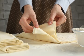 Woman with puff pastry dough at white table, closeup