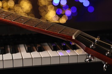 Fototapeta premium Guitar on piano against blurred lights, closeup. Bokeh effect