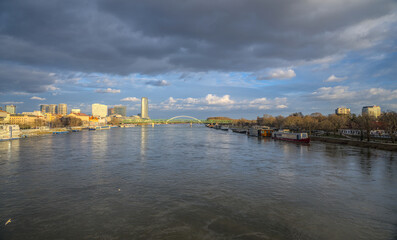 Fototapeta premium Wide view of a river surrounded by a modern cityscape and cloudy skies.