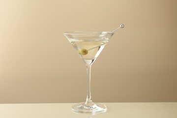 Martini cocktail with olive in glass on beige table