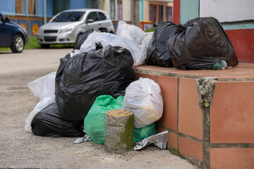 Plastic trash bags with household garbage put out on residential street by house porch for collection.