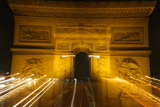 The illuminated Arc de Triomphe in Paris captured at night with light trails at slow shutters speed creates a dramatic effect, highlighting the historic monument and the vibrancy of the Champs-Élysées