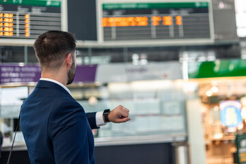 copyspace businessman checks wristwatch while looking at station information panels