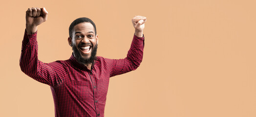 Winner Concept. Studio portrait of african american man yelling with clenched fists raised up in the air, isolated over yellow studio background. Black guy cheering and screaming, celebrating victory