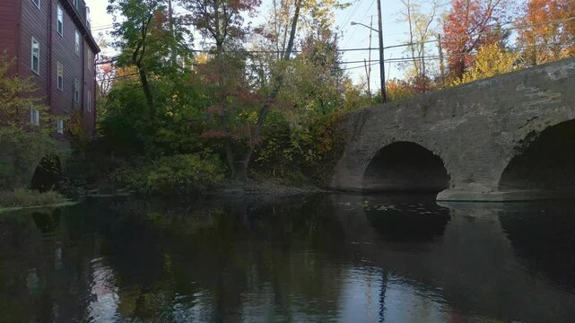 Old stone bridge and historic mill on a tranquil river with Fall foliage during golden hour, drone 4K