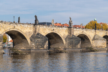 Fototapeta premium Charles Bridge spans the Vltava River in Prague, featuring Gothic architecture and statues. Autumn colors enhance its reflection in the calm water.