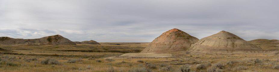 Panorama of low muddy hills in a dry grassy ranch setting with a cloudy sky
