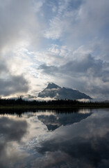 Vertical panorama of a mountain reflecting in a calm lake with morning mist and clouds
