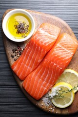 Pieces of fresh salmon with thyme, lemon, oil and spices on black table, top view