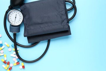 Blood pressure measuring device and pills on light blue background, top view. Space for text