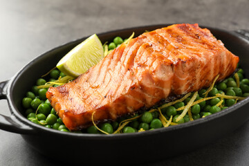 Delicious grilled salmon fillet with green peas and lime in baking dish on grey table, closeup