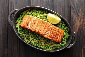 Delicious grilled salmon fillet with green peas and lime in baking dish on wooden table, top view