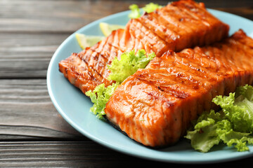 Delicious grilled salmon fillets with lettuce on wooden table, closeup