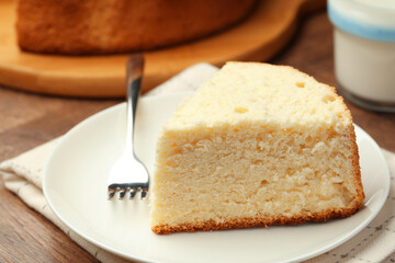 Piece of delicious sponge cake and fork on wooden table, closeup