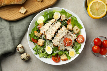Tasty Caesar salad with chicken and tomatoes in bowl on gray textured table, flat lay