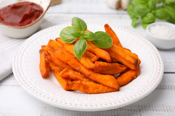 Sweet potato fries and basil on light wooden table, closeup