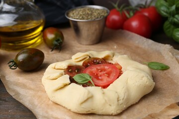 Raw galette with tomato and basil on wooden table, closeup