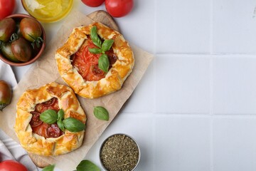 Tasty galettes with tomato and basil on white tiled table, flat lay. Space for text